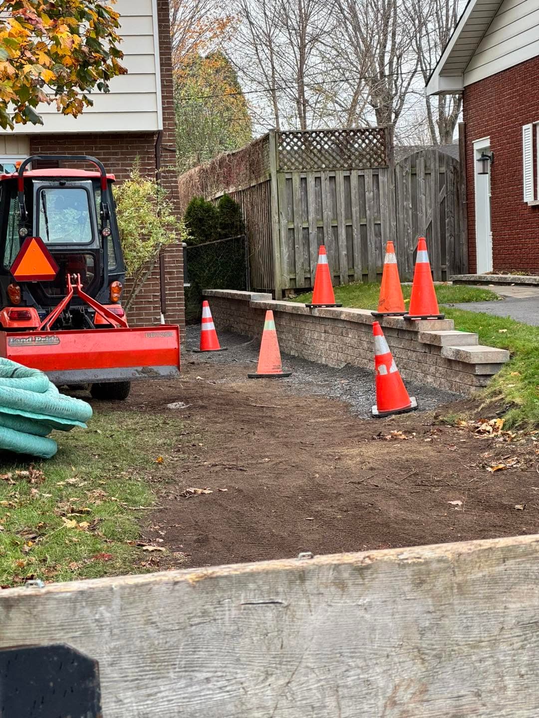 Compact tractor grading a backyard beside a retaining wall
