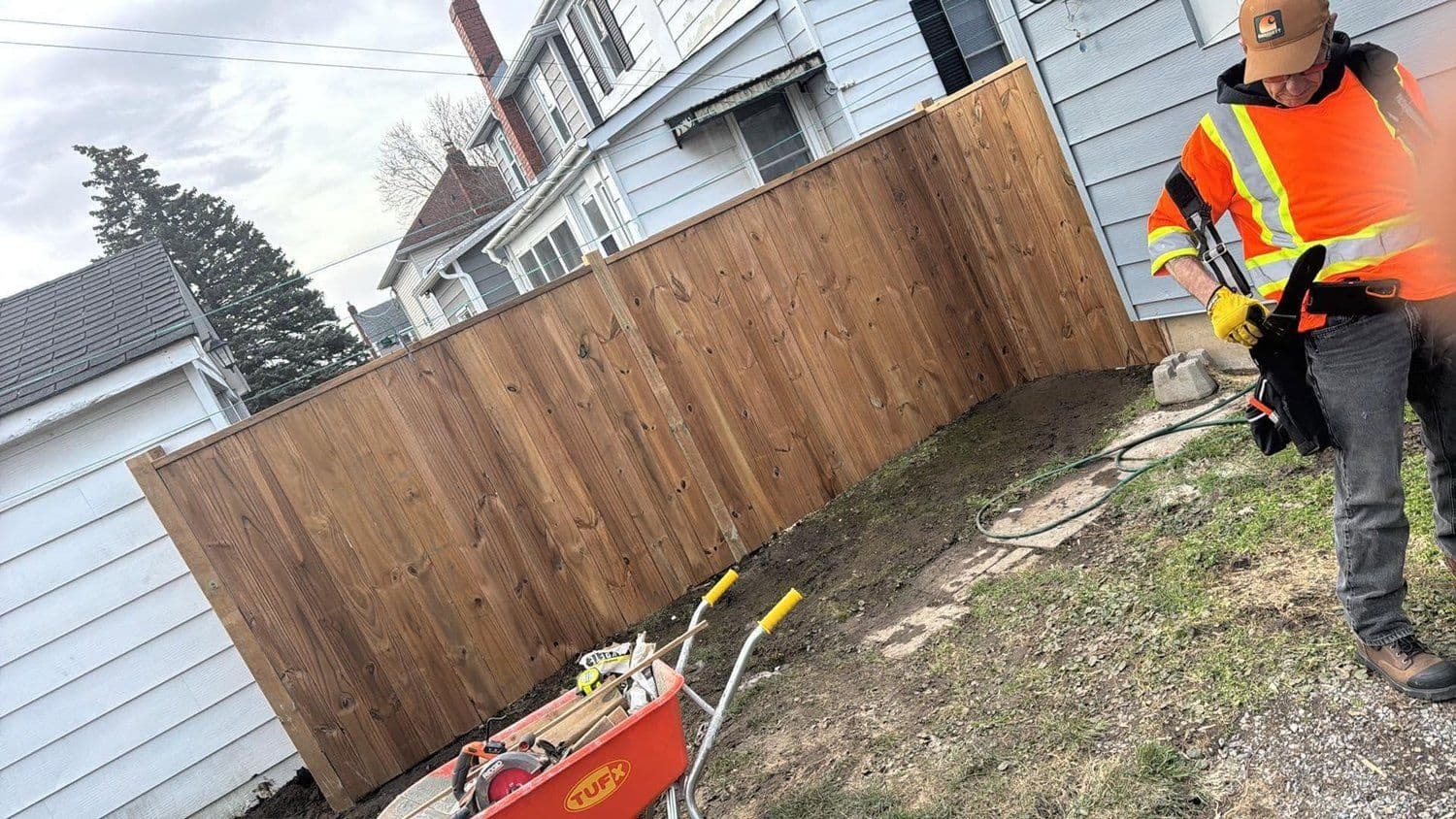 BHOSS crew member in high-visibility gear building a wood privacy fence